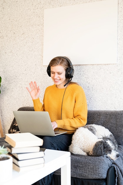 Photo distance learning. e-learning. young smiling woman in yellow sweater and black headphones studying online using laptop, sitting on the couch at home