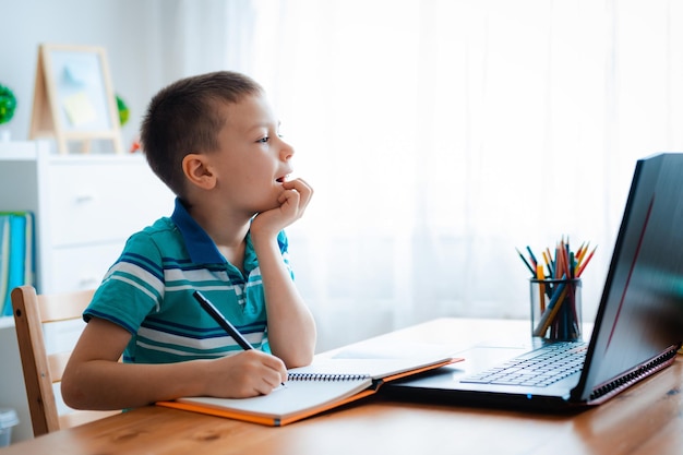 Distance learning online education A schoolboy boy studies at home and does school homework A home distance learning