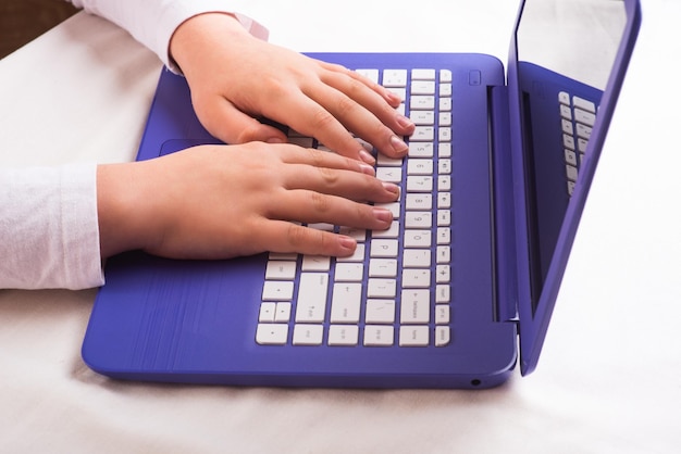 Дистанционное обучение онлайн образование. Болезненный школьник учится дома с синим ноутбуком на столе, делает домашнее задание. Крупный план