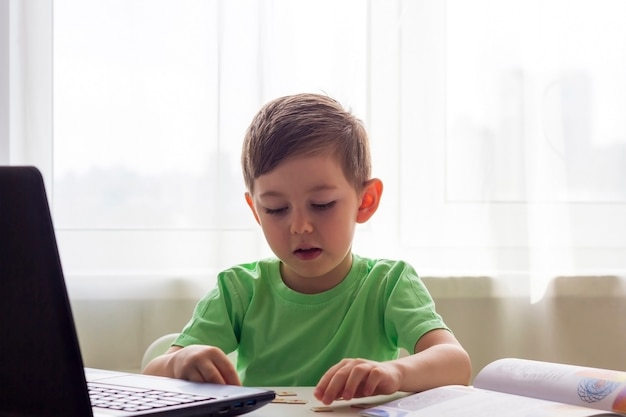 Apprendimento a distanza, istruzione online. distanza sociale e autoisolamento durante la quarantena. bambino in età prescolare o scolaro che studia a casa con il taccuino e che fa i compiti per la scuola di sviluppo.