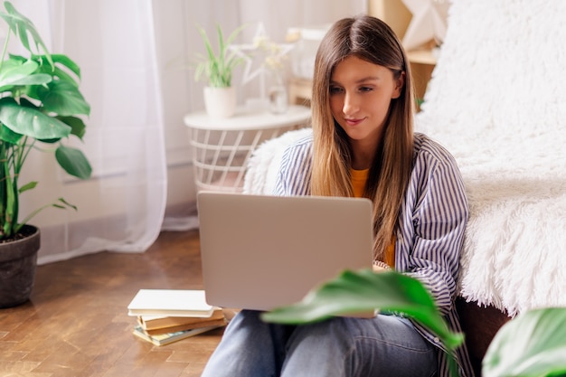 Distance learning online education and work. Business woman typing at laptop, sitting on the floor near the plants and books.