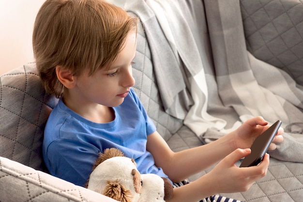 Formazione a distanza online e lavoro. il bambino studia da remoto da casa. le mani del ragazzo tengono il telefono cellulare