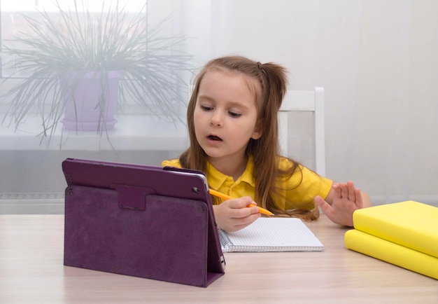 Distance learning online-home education. A schoolgirl is studying with a digital tablet and doing school homework. Study books and notebooks on the table.