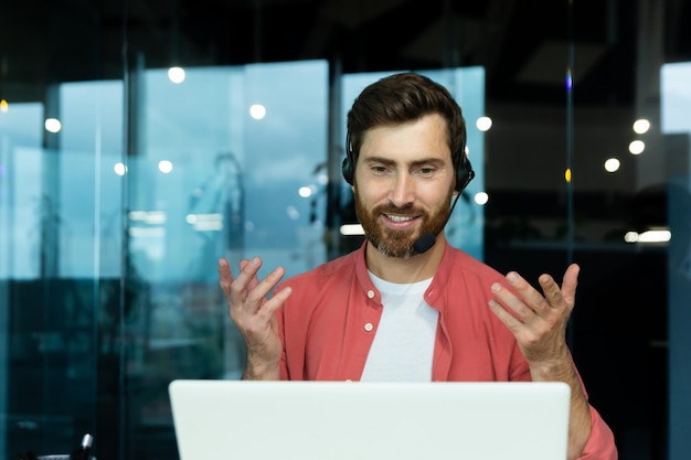 Distance learning portrait of a young man teacher in a headset in a red shirt sits in the office at