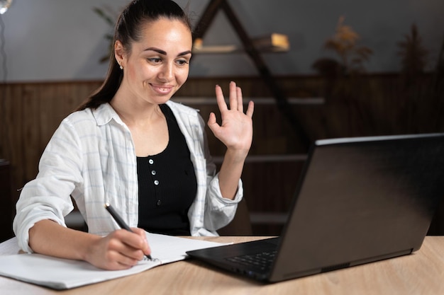 Distance learning teacher with laptop sitting in home office\
using wireless technologies for lessons webinars remote tutor is in\
touch with students in the zoom remote education concept