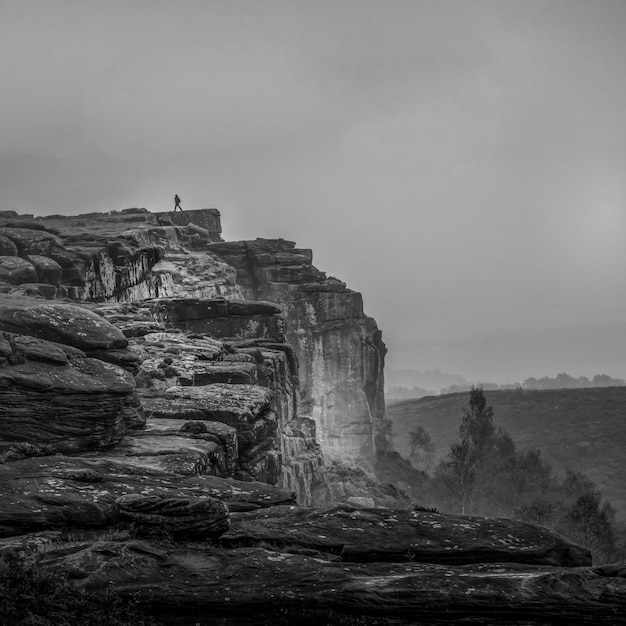 Foto vista in distanza di un uomo in piedi su una scogliera contro il cielo