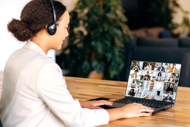 사진 원격 교육, 원격 직업 및 사람 개념: 노트북 컴퓨터와 헤드폰을 착용한 여성 학생, 가정 사무실에서 비디오 통화 또는 온라인 수업을 하고 손을 흔들고 있습니다.