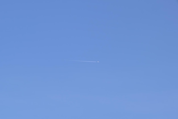 Distant passenger jet plane flying on high altitude on clear blue sky leaving white smoke trace of contrail behind Air transportation concept