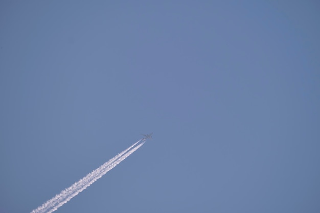 Distant passenger jet plane flying on high altitude on clear blue sky leaving white smoke trace of contrail behind Air transportation concept