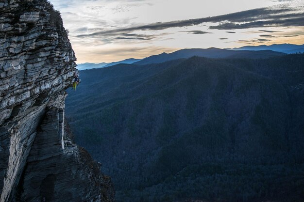 Photo distant view of man rock climbing against mountains during sunset