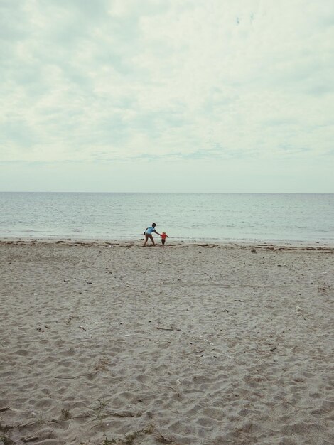 사진 흐린 하늘 을 배경 으로 해변 에서 놀고 있는 여자 와 소년 의 멀리 있는 모습