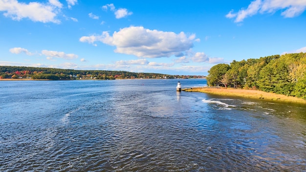 Distant view over river of small lighthouse in Maine with fall foliage