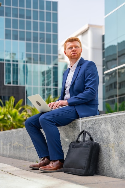 Photo distracted businessman sitting outside a financial building using laptop