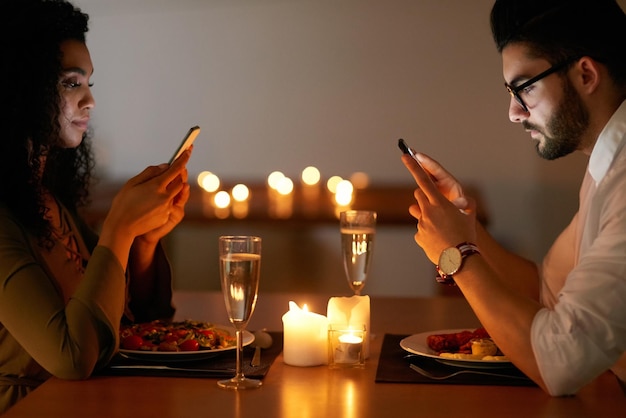 夕食に気を取られて夕食に出かけている間に彼らの電話でテキストメッセージを送る若いカップルのショット
