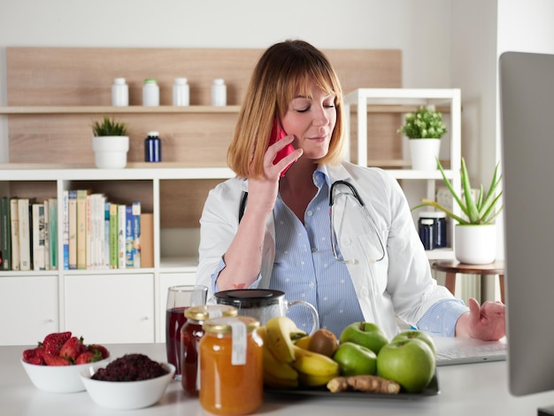 Nutrizionista femminile distratto che chiacchiera con lo smartphone nello studio dell'ufficio