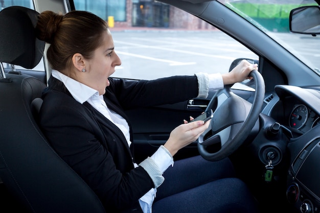 車の運転中にスマートフォンを使用して気が散る女性