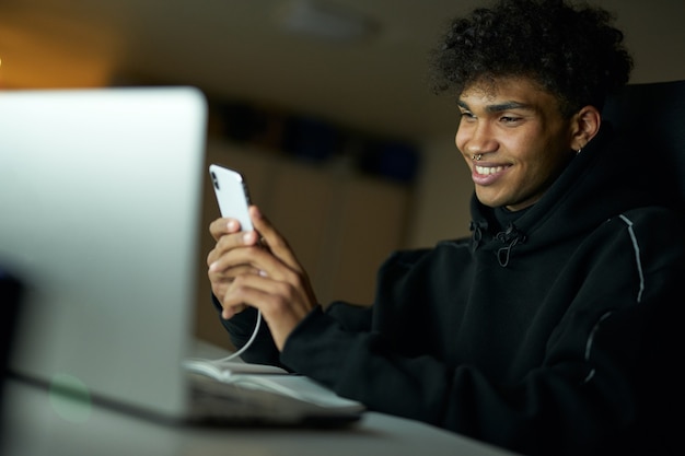 Distraction portrait of happy male student smiling and using smartphone while studying working on