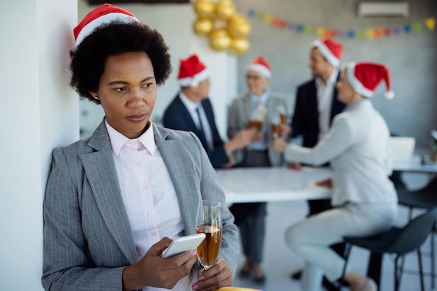 Distraught black businesswoman texting on cell phone during Christmas office party