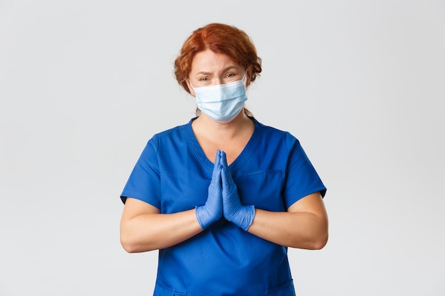  Distressed begging redhead female doctor in face mask and rubber gloves pleading, supplicating, cry for help 