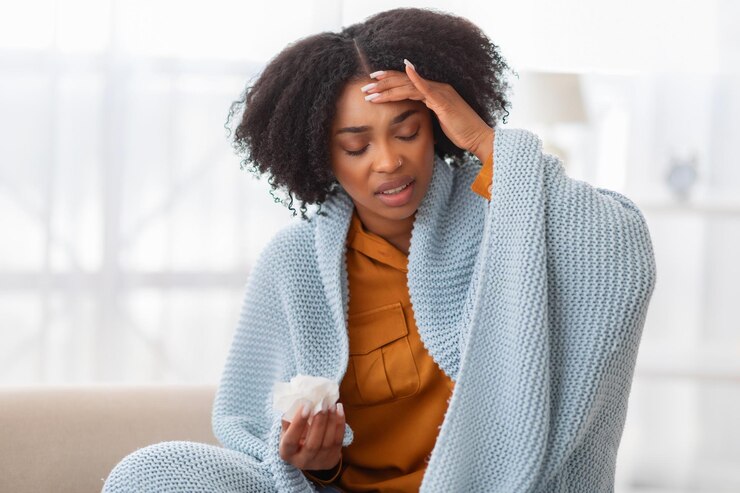 Photo distressed young woman with curly hair sitting on a couch wrapped in a blue blanket