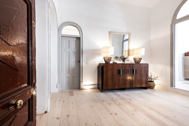 Distributor corridor of a house with eclectic decoration with white wood carpentry vintage wood and marble locker rococo goldframed mirror and gray fabric armchair