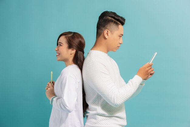 Distrust Concept. Beautiful young modern couple with smartphones in hands standing back to back.