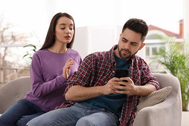 Distrustful young woman peering into boyfriend39s smartphone at home