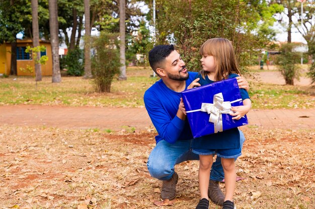 Dit cadeau is voor jou portret van een liefdevol meisje naast vader dat hem begroet met vaderdag of verjaardag met ingepakte geschenkdoos gelukkige familievakantie samen in het park