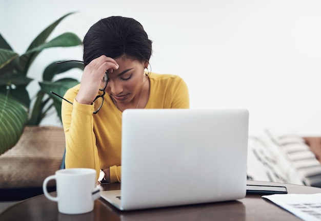 Dit gaat niet zo goed Shot van een aantrekkelijke jonge vrouw die alleen thuis zit en hoofdpijn heeft terwijl ze haar laptop gebruikt