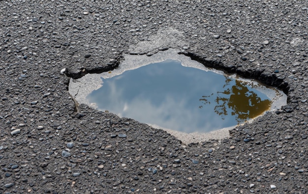 Dit gat in de weg dat nu met water is gevuld, accentueert de onvolkomenheden van de weg