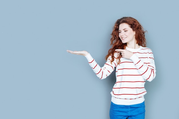 Dit is het. Leuke vrolijke positieve vrouw die lacht en naar haar hand kijkt terwijl ze naar het virtuele object wijst