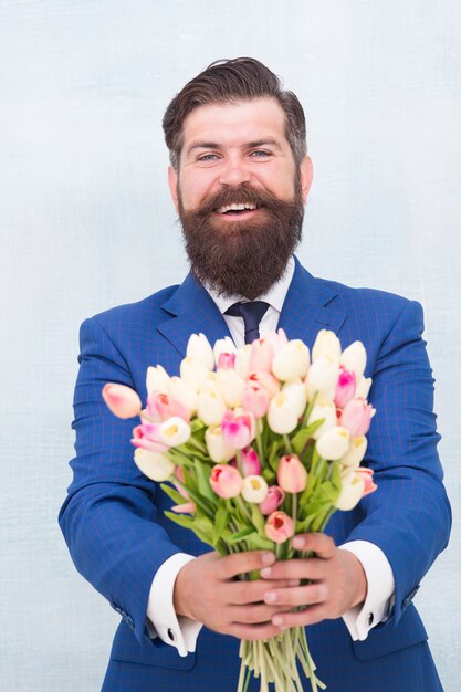 Dit is voor jou. Vrouwendag. 8 maart. Lente cadeau. Bebaarde man hipster met bloemen. Vier de lente. Verrassing maken. Heer met tulpen. De lente komt eraan. De groeten. Bebaarde man tulpenboeket.