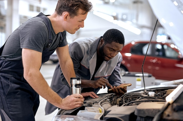 Foto diverse blanke en zwarte mannen mechanische inspectie controleren bug in motor van applicatie smartpho