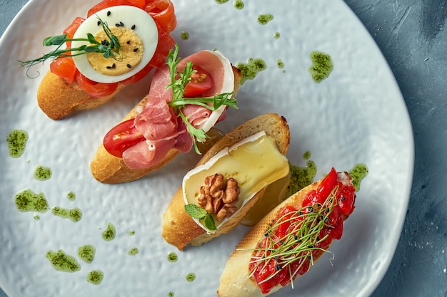 Diverse bruschetta met gebakken paprika, camembert, prosciutto en licht gezouten zalm in een witte plaat