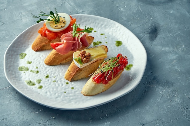 Diverse bruschetta met gebakken paprika, camembert, prosciutto en licht gezouten zalm in een witte plaat