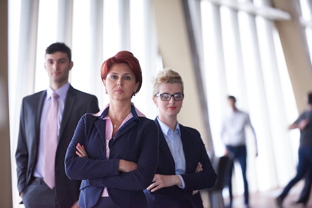 リーダーとして前に赤毛の年配の女性とモダンな明るいオフィスのインテリアでチームとして一緒に立っている多様なビジネスの人々のグループ