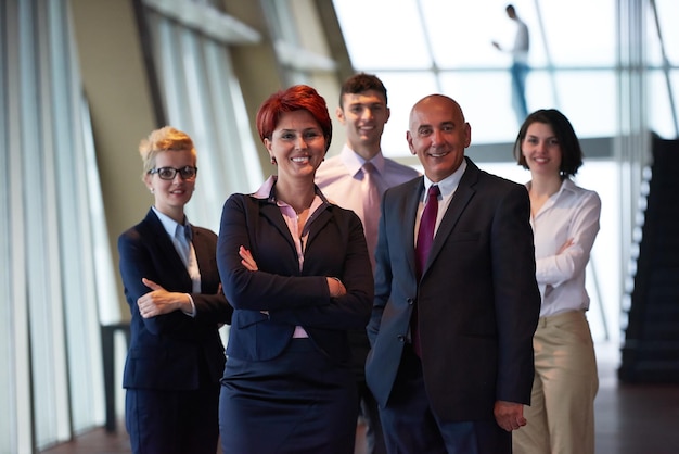 Diversi gruppi di uomini d'affari in piedi insieme come squadra in interni moderni e luminosi dell'ufficio con una donna senior dai capelli rossi di fronte come leader