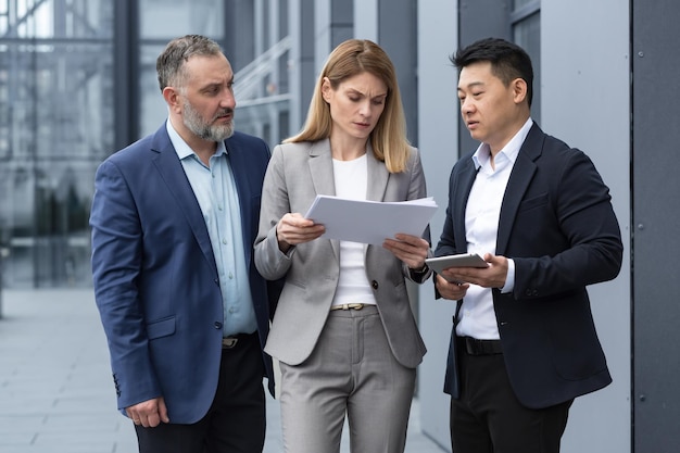 Diverse business team three colleagues employees discuss documents contract outside office building