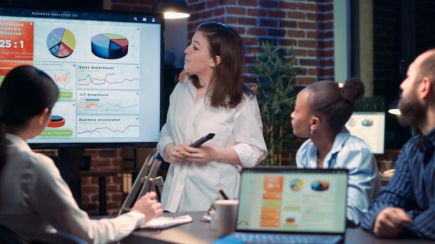 Diverse businesswomen in business meeting, employee presenting analytics research, showing statistics on digital board screen. Office worker marketing report presentation, strategy planning