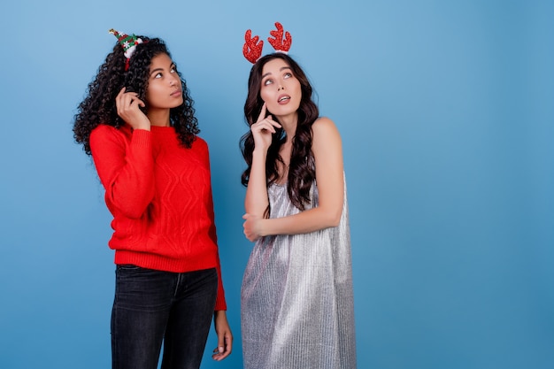 Diverse caucasian and black women wearing holiday hoops isolated over blue