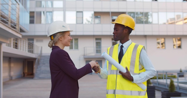 Diverse contractor and architect shaking hands outside construction site