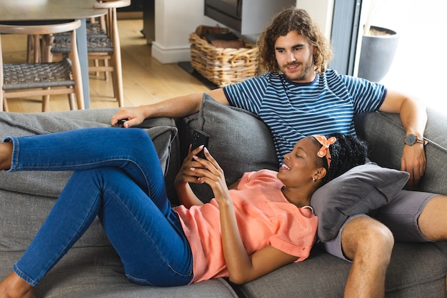 Diverse couple young African American woman and Caucasian man relax on a sofa browsing a smartphone