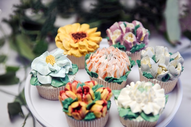 Diverse cupcakes versierd met kleurrijke bloemensuikerglazuur op witte cupcakestandaard en tafel voor partyflo