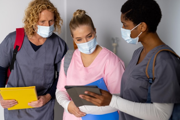 Diverse doctors wearing face masks discussing work and using tablet in corridor at hospital