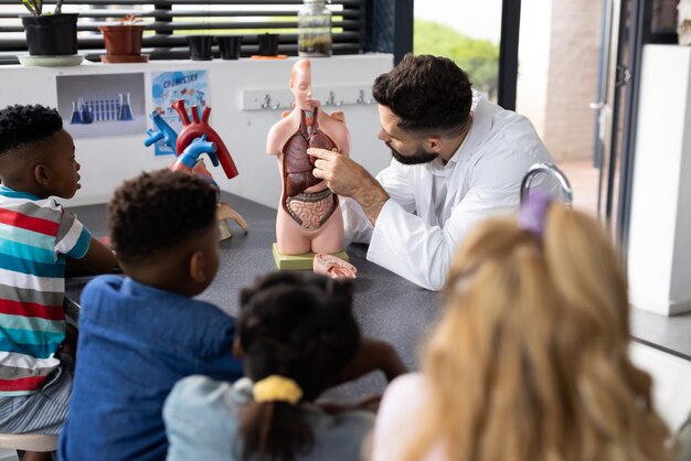 Foto diversi alunni della scuola elementare e un insegnante di biologia maschio che studiano il modello del corpo umano nello spazio di copia