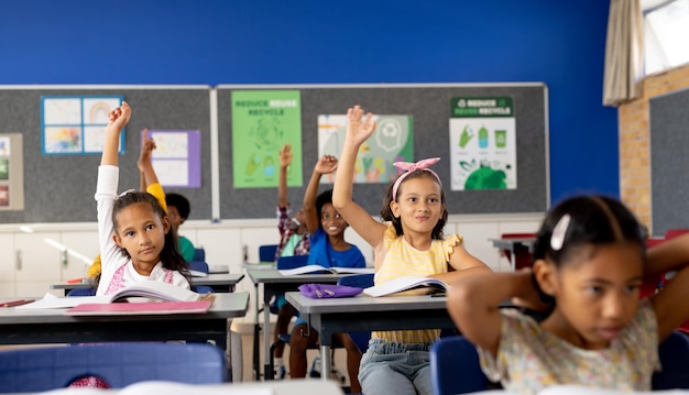 写真 さまざまな小学生が教室で机に座って手を挙げている