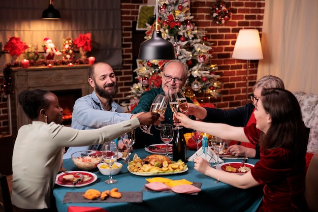 Diverse familie rammelende glazen met mousserende wijn, kersttoast voorstellen, drinken tijdens een feestelijk diner. Wintervakantieviering met ouders, mensen die samenkomen