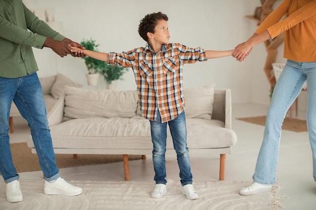 Diverse father and mother pulling son in different sides indoor