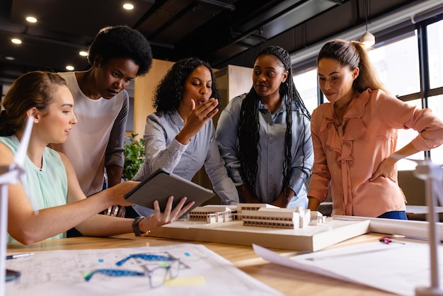 Photo diverse female architects in discussion using model, blueprints and tablet in casual office meeting. casual office, teamwork, business, lifestyle, creative work, communication and work, unaltered.