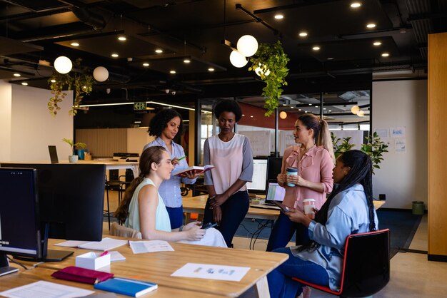 Photo diverse female colleagues in discussion using tablet in casual office meeting. casual office, teamwork, business, lifestyle, communication and work, unaltered.